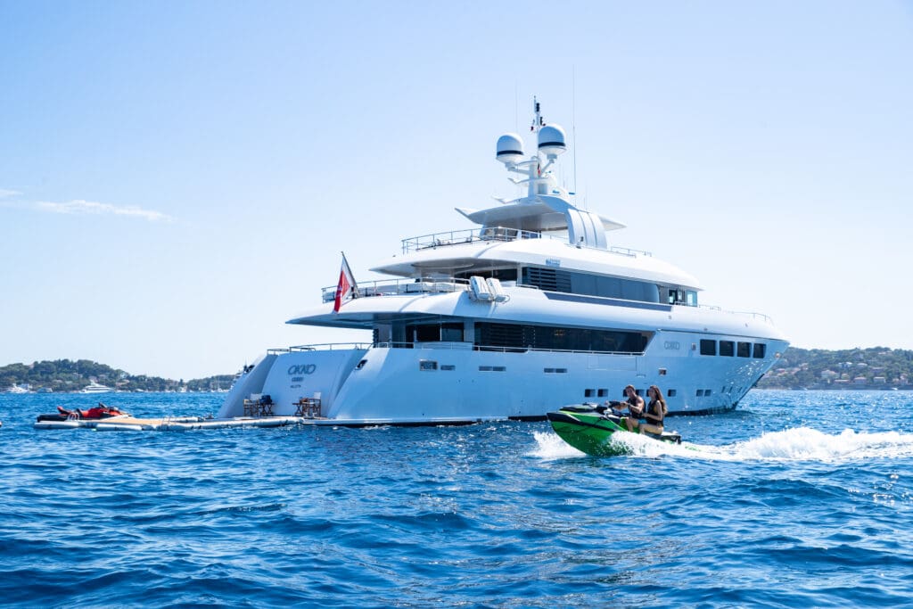 A couple riding a jet ski next to a large yacht.